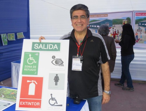 Miembro de la brigada comunitaria del Rimác, en una feria mostrando señaléticas de zona segura, extintores y personas con discapacidad.